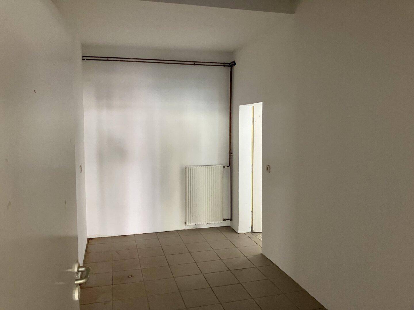 Einfacher Raum mit Fliesenboden und sichtbaren Rohren, geeignet als Lager oder Nebenraum.