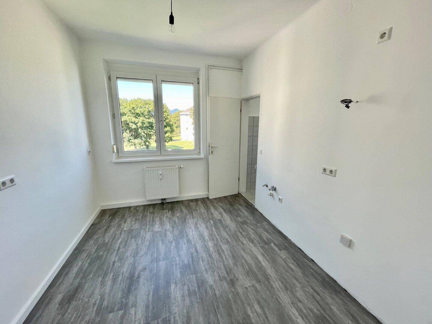 Leeres Zimmer mit modernem Vinylboden, weißen Wänden und Zugang zu einem Bad.