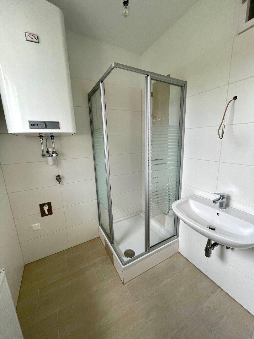 Funktionales Badezimmer mit Duschkabine, Waschbecken und Warmwasserboiler an der Wand.