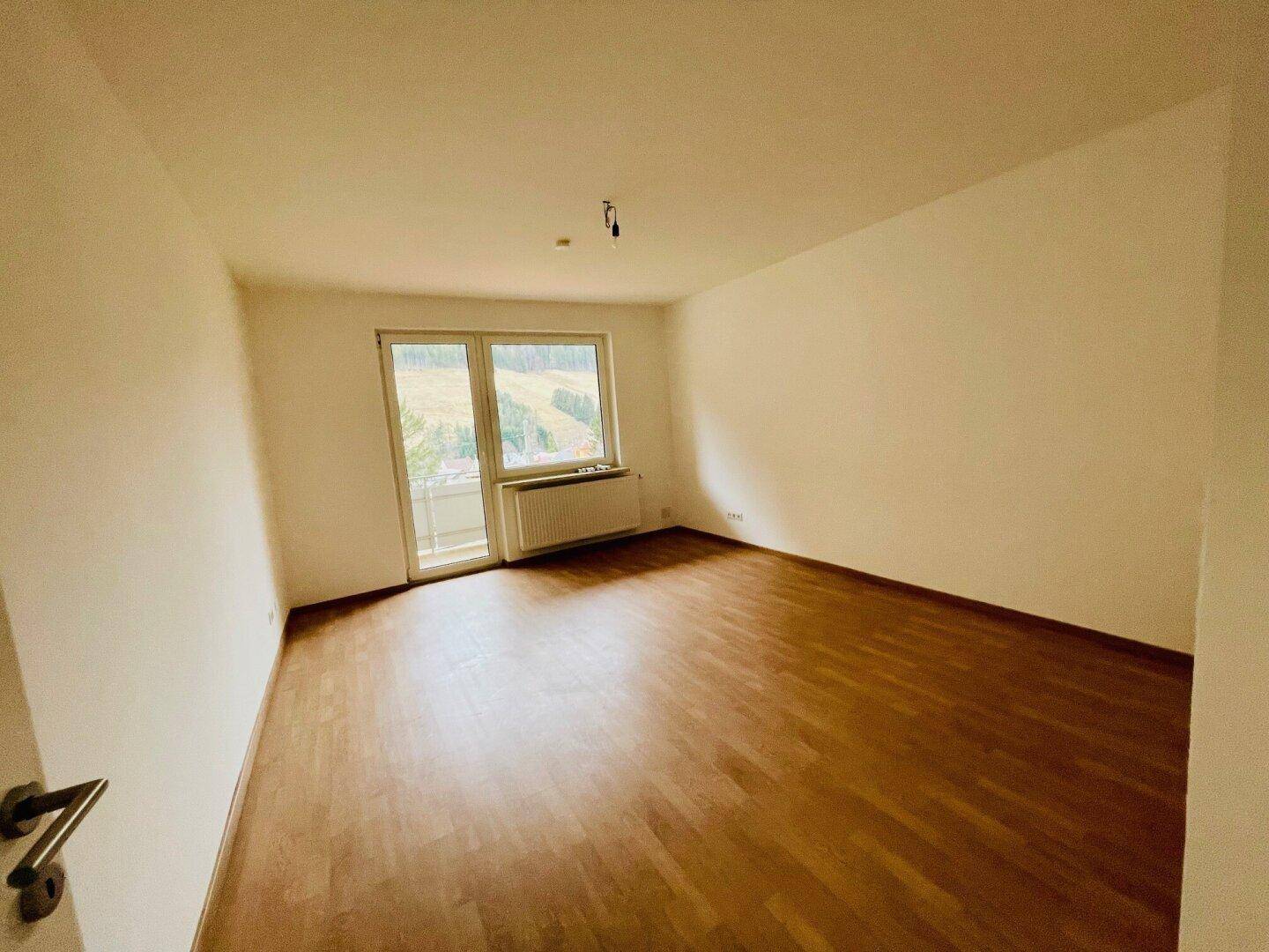 Heller Wohnraum mit Holzboden, weißen Wänden und Zugang zu einem Balkon mit Bergblick.