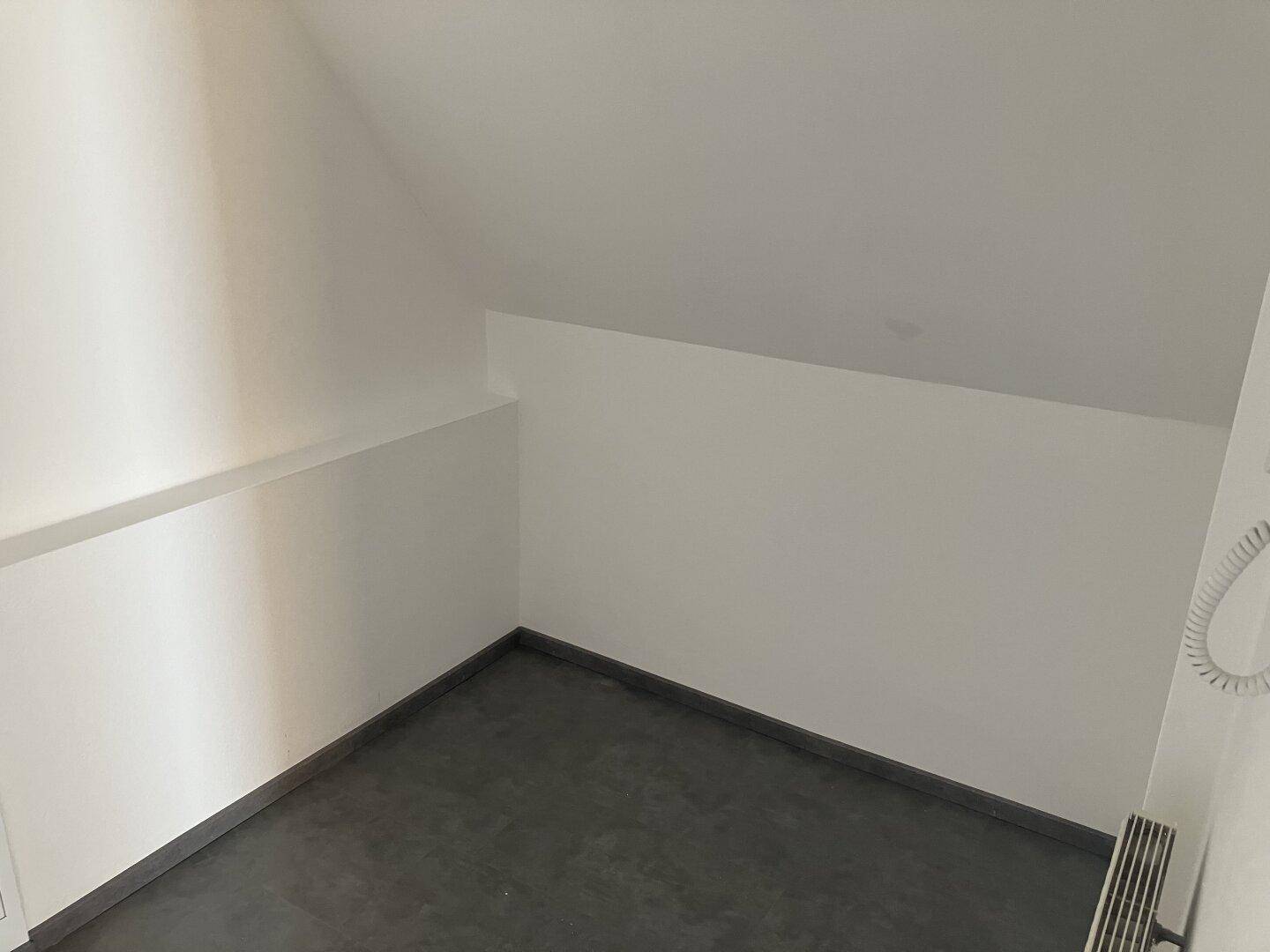 Kleiner Raum mit dunklem Fliesenboden und schrägen Wänden im Dachgeschoss.