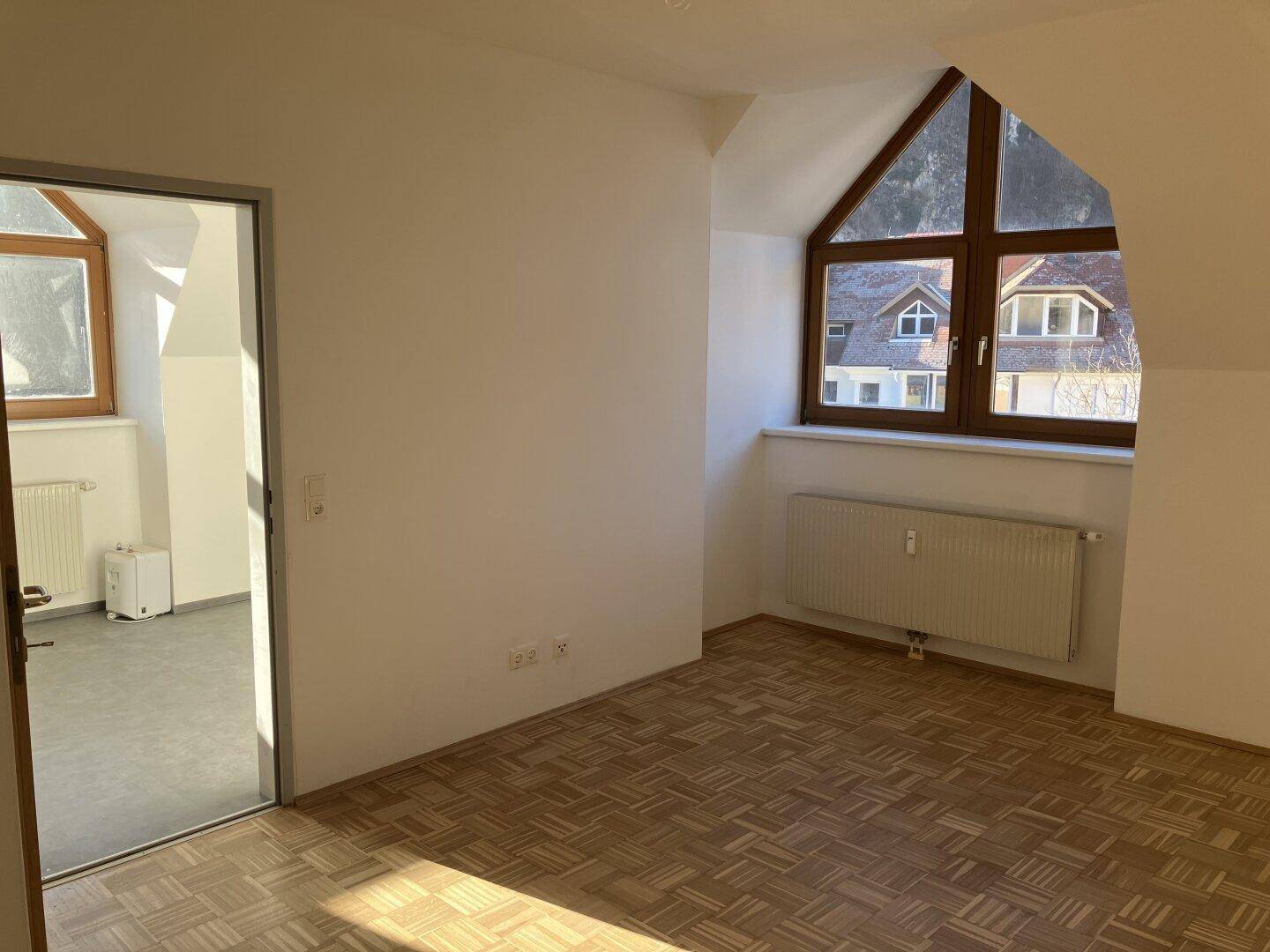 Geräumiger Dachgeschossraum mit Parkettboden, schrägen Wänden und Zugang zu einem weiteren Zimmer.