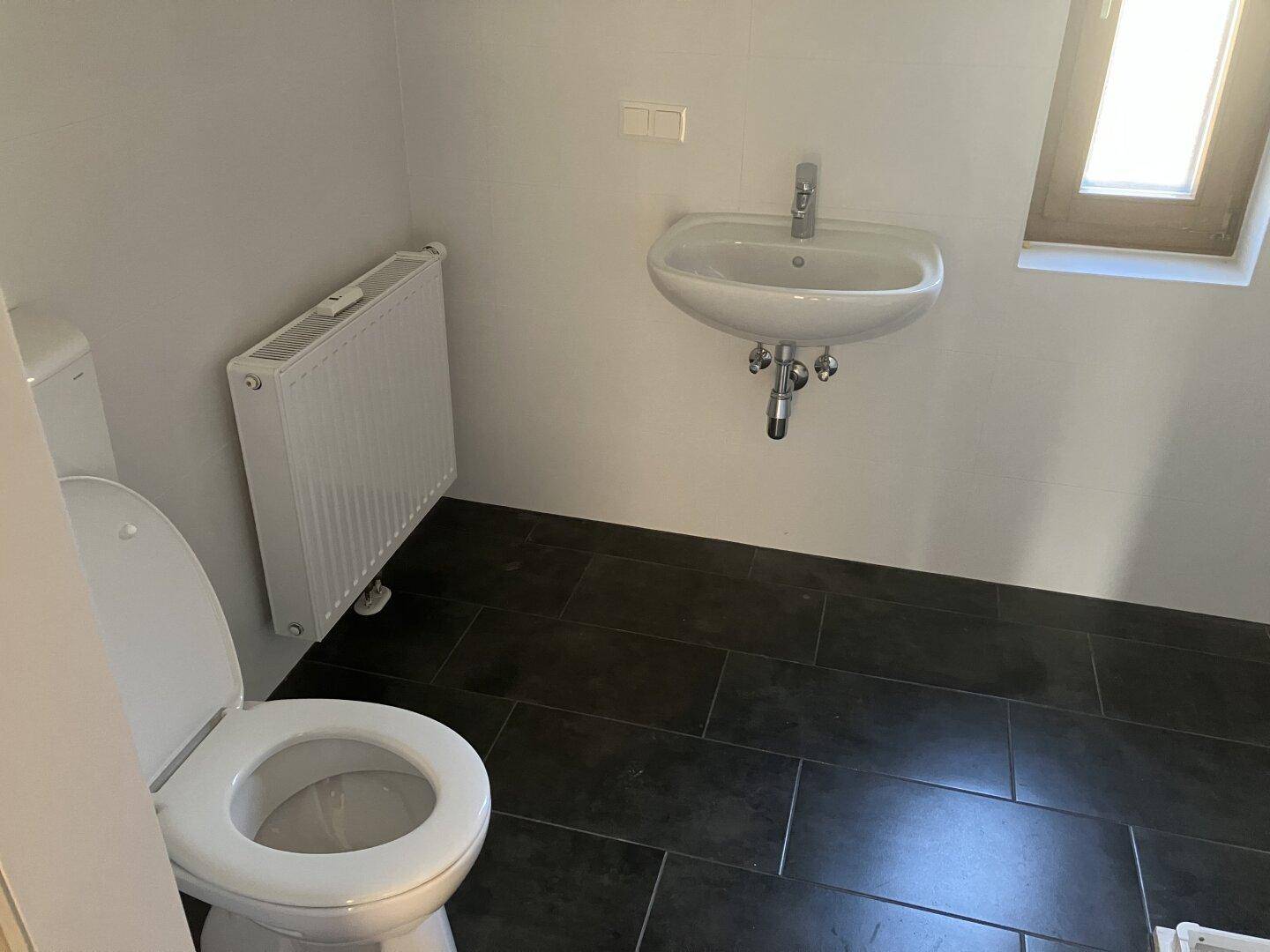 Funktionales Badezimmer mit WC, Waschbecken, Heizkörper und kleinem Fenster.