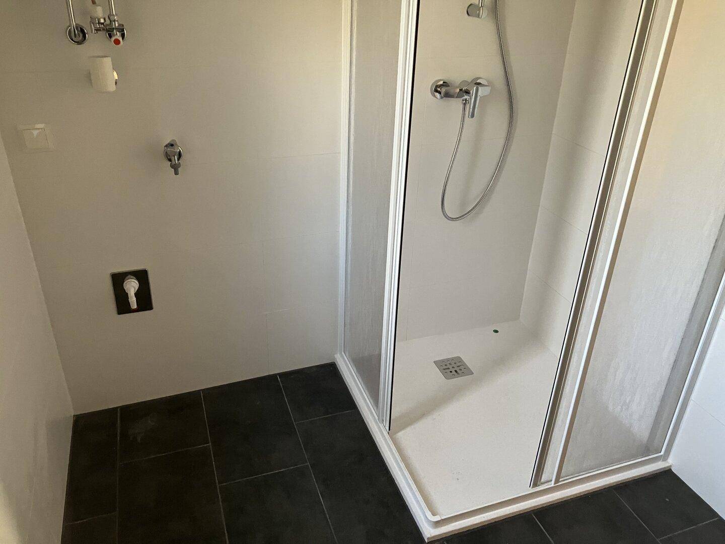 Badezimmer mit Duschkabine und dunklem Fliesenboden, bereit für die Nutzung.