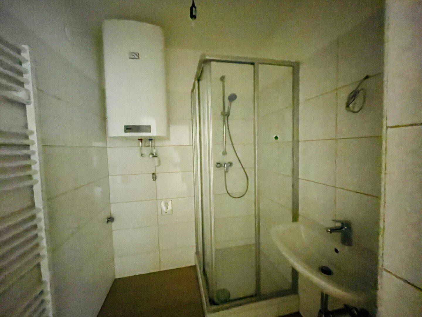 Kleines Badezimmer mit Duschkabine, Waschbecken, Wandfliesen und einem Handtuchheizkörper.
