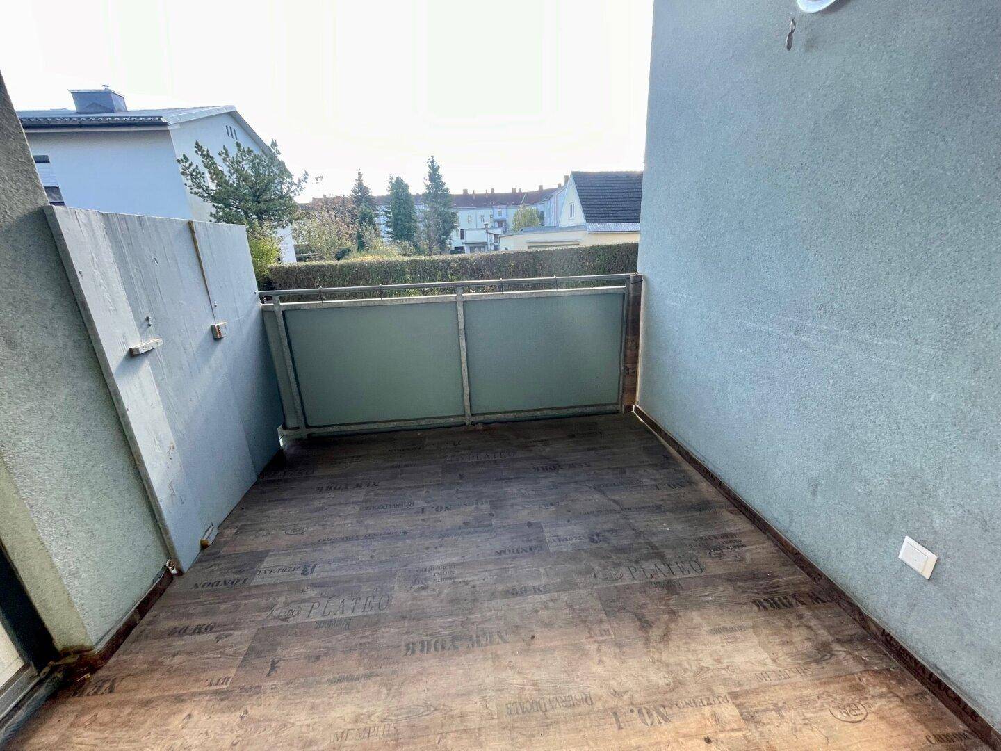 Sonniger Balkon mit Holzbodenoptik und Blick auf die Umgebung.
