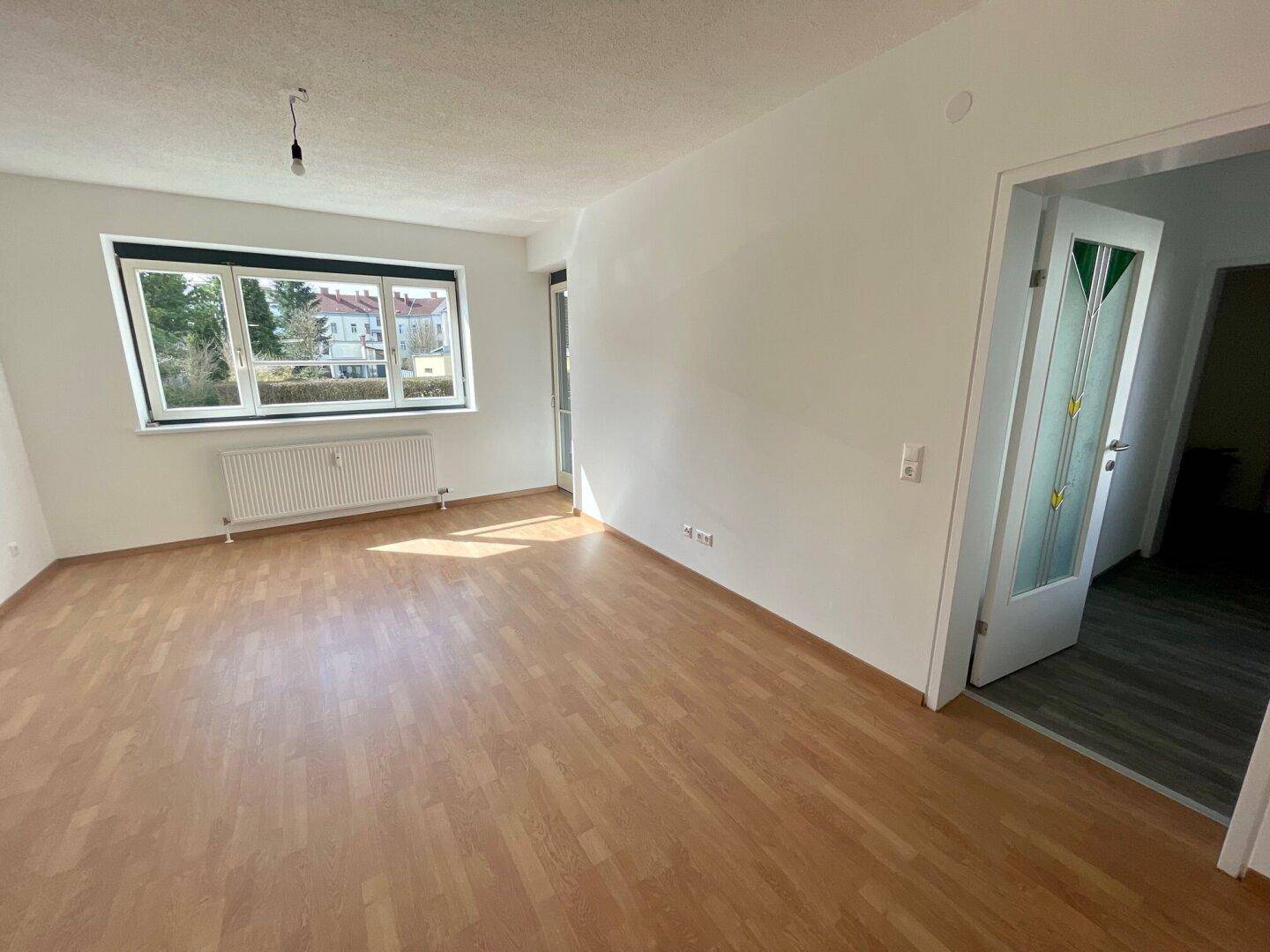 Geräumiges Zimmer mit hellem Laminatboden und Zugang zu einem weiteren Bereich.