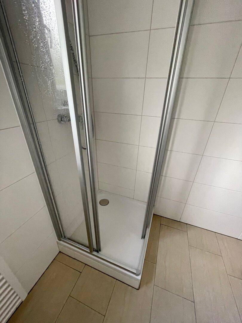 Duschkabine mit Glaswänden und weißen Fliesen im Badezimmer.
