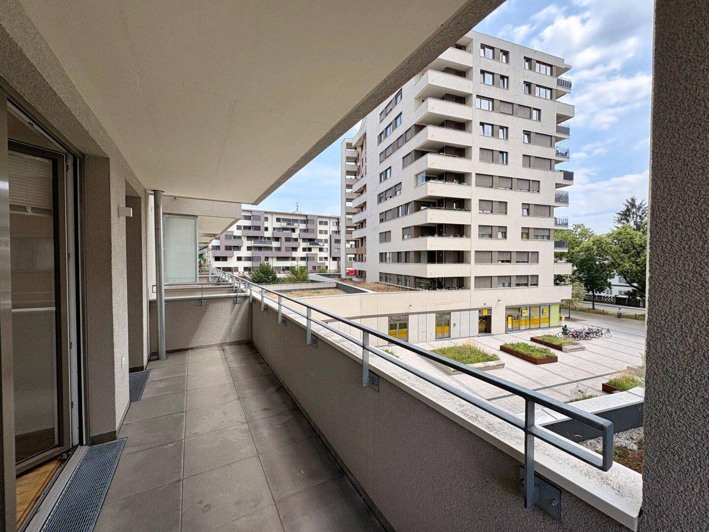 Geräumiger Balkon mit Fliesenboden und Blick auf die umliegenden modernen Gebäude und den Innenhof.