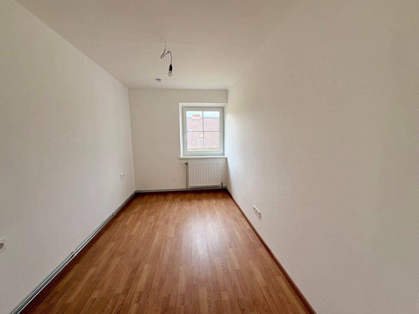 Heller Raum mit Laminatboden, weißen Wänden und einem Fenster, bereit zur Einrichtung.