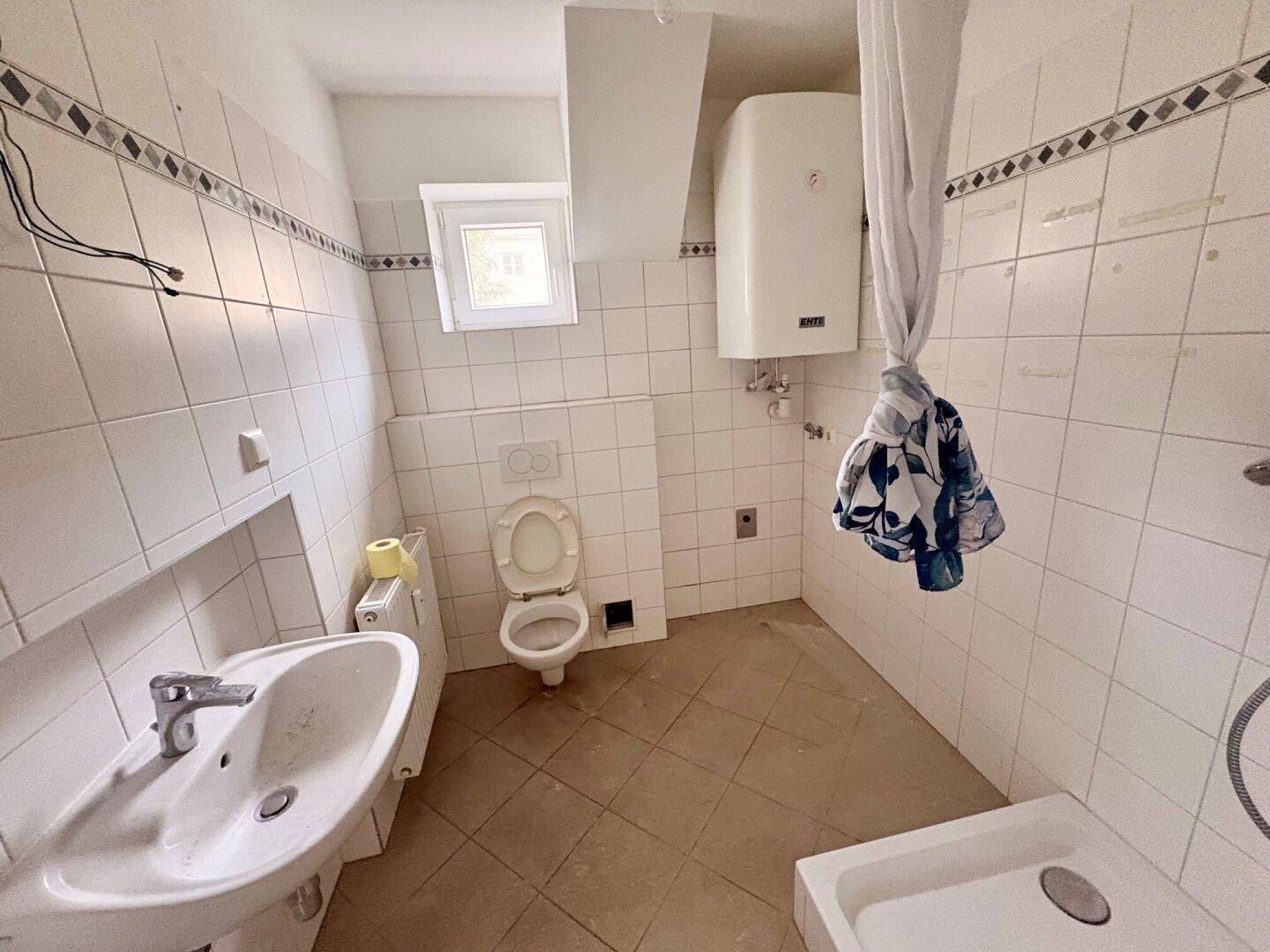 Badezimmer mit weißen Fliesen, Dusche, WC, Bidet und einem kleinen Fenster für Tageslicht.