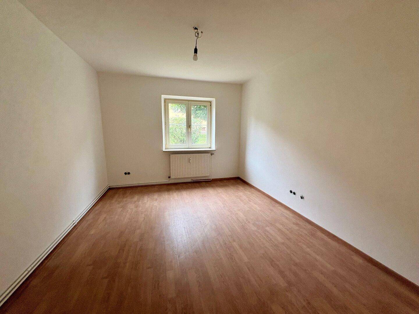Leeres Zimmer mit braunem Laminatboden und einem Fenster, ideal für ein Schlafzimmer oder Büro.