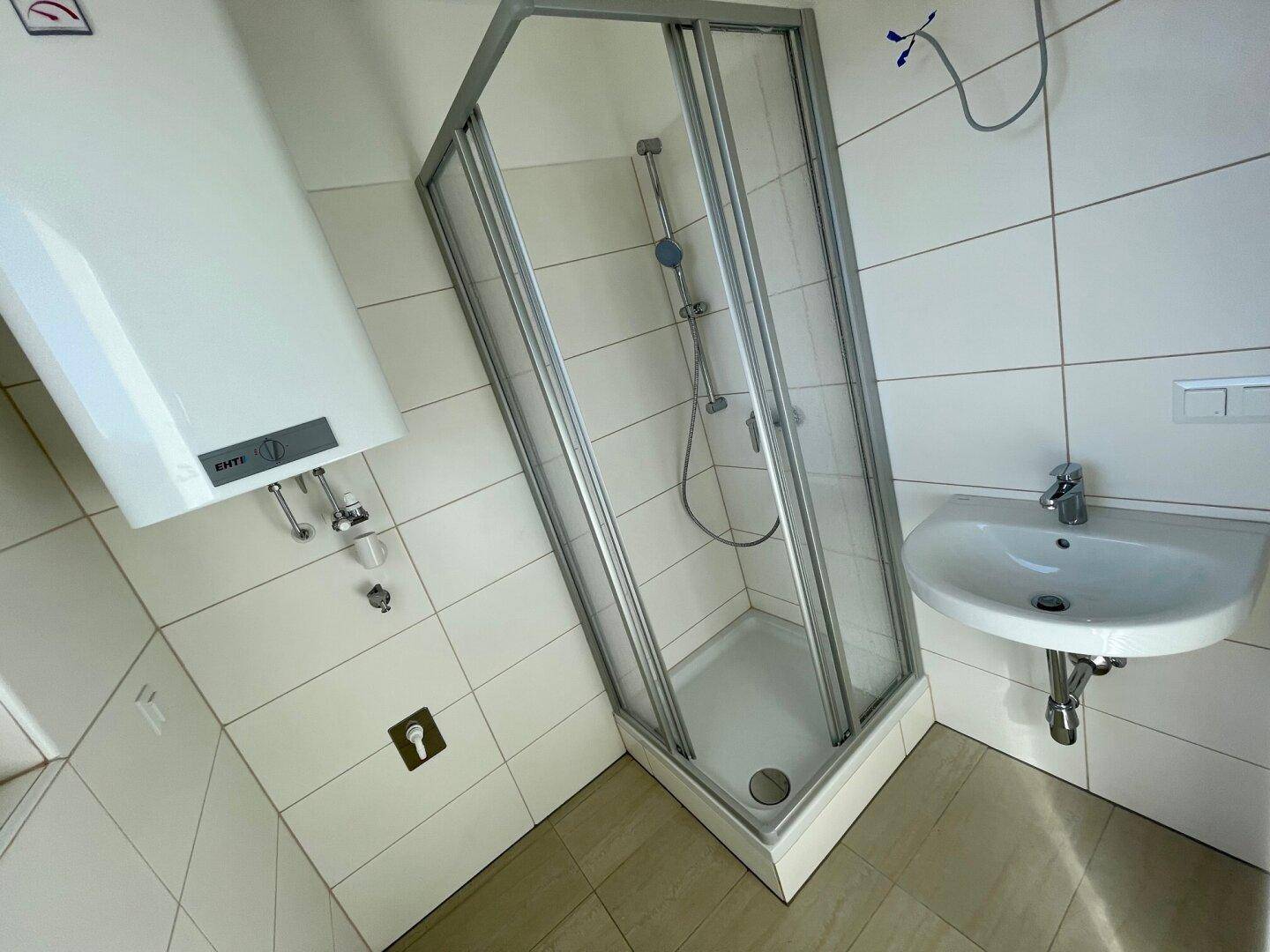 Funktionales Badezimmer mit weißen Fliesen, Duschkabine und Waschbecken.