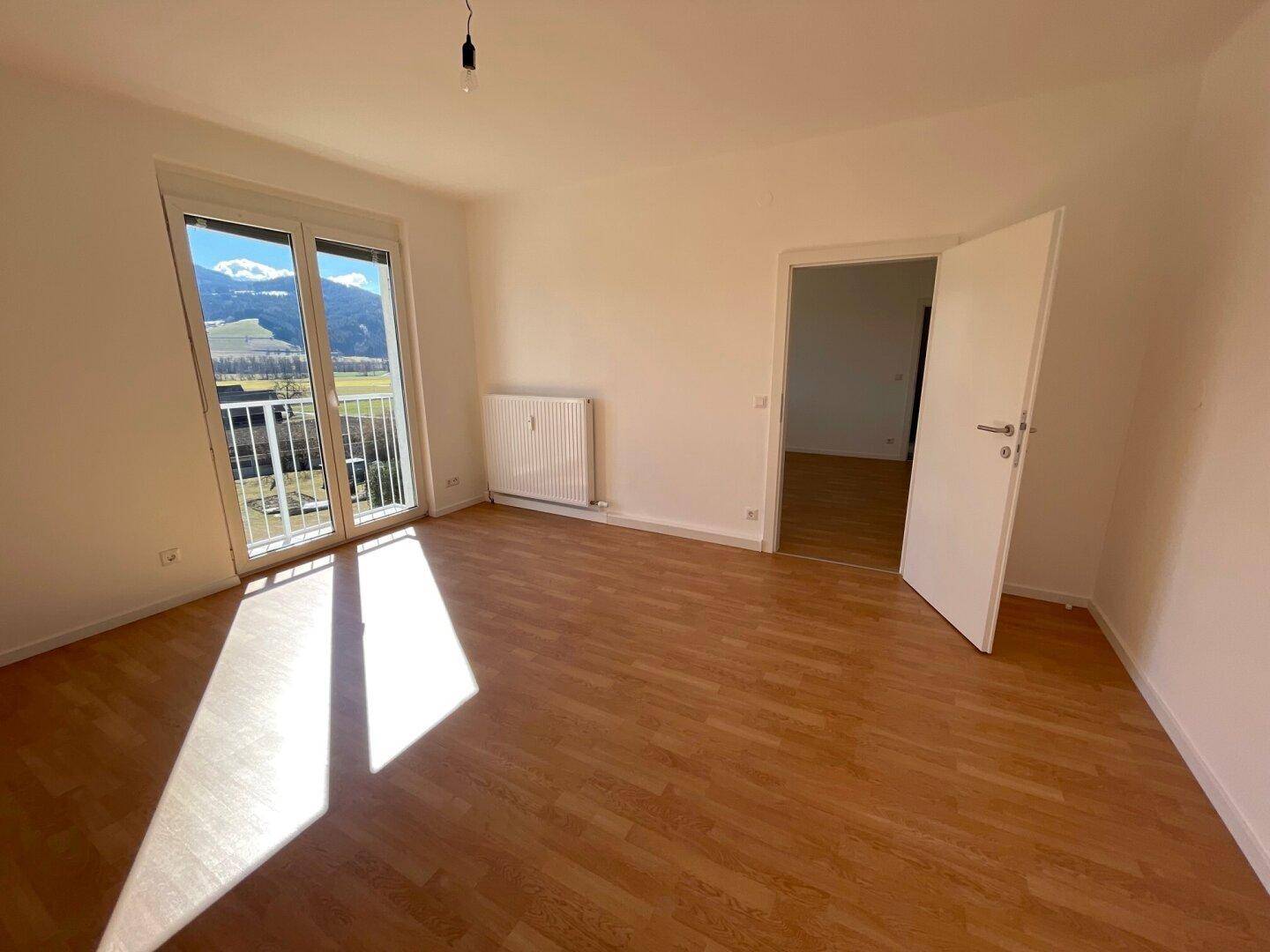 Lichtdurchflutetes Zimmer mit Holzboden, Bergblick und offener Tür zu einem weiteren Raum.