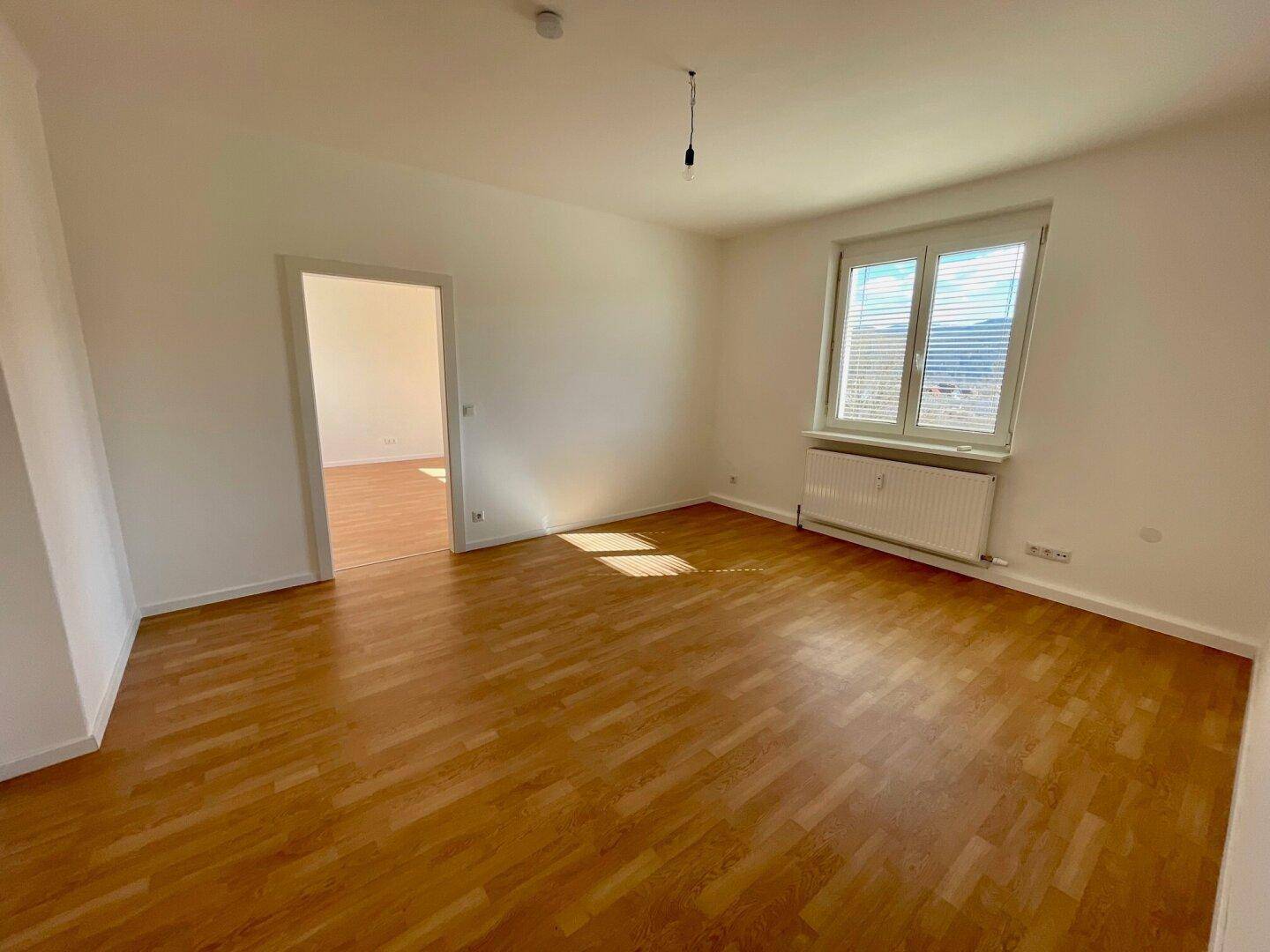 Helles Zimmer mit Holzboden, Heizkörper und Fenster mit Blick auf die umliegende Berglandschaft.