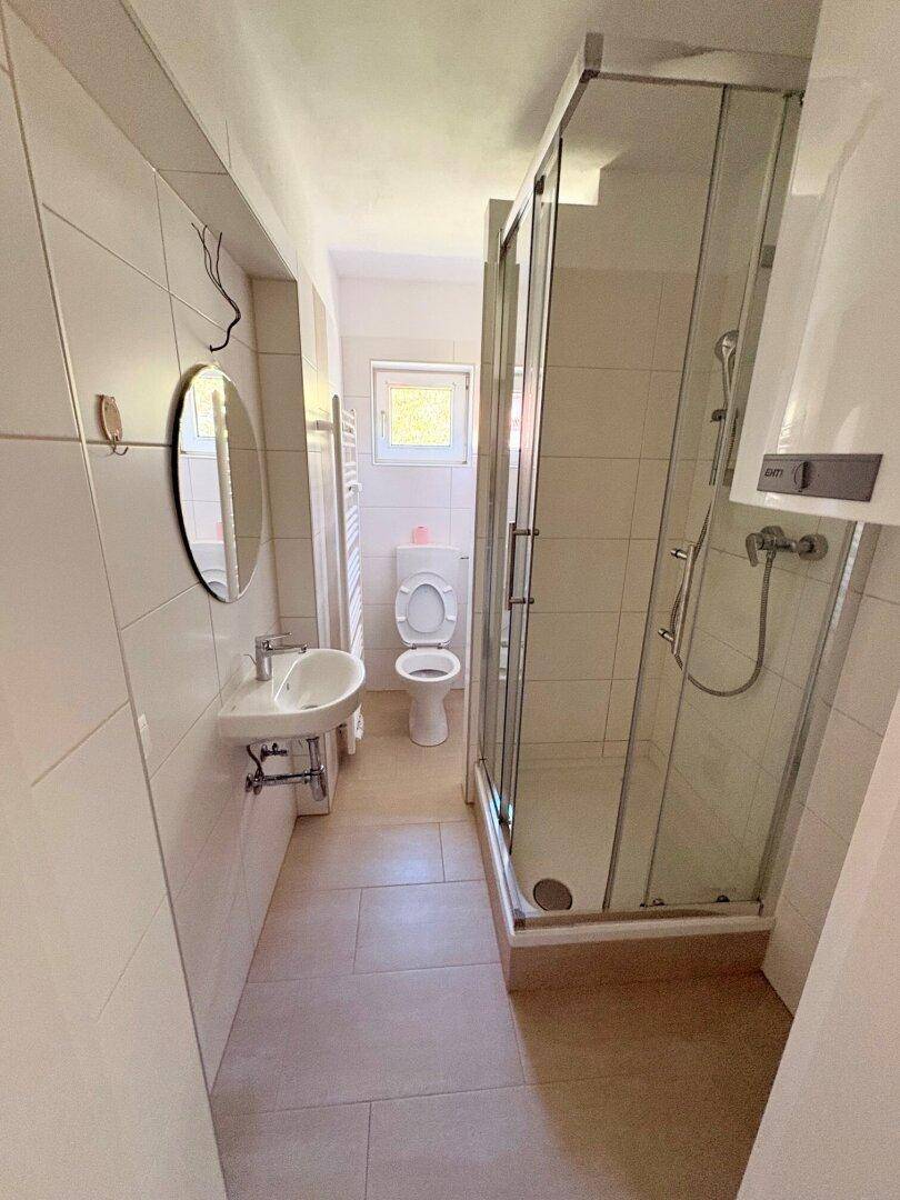 Helles Badezimmer mit Duschkabine, WC, Waschbecken und Fenster.