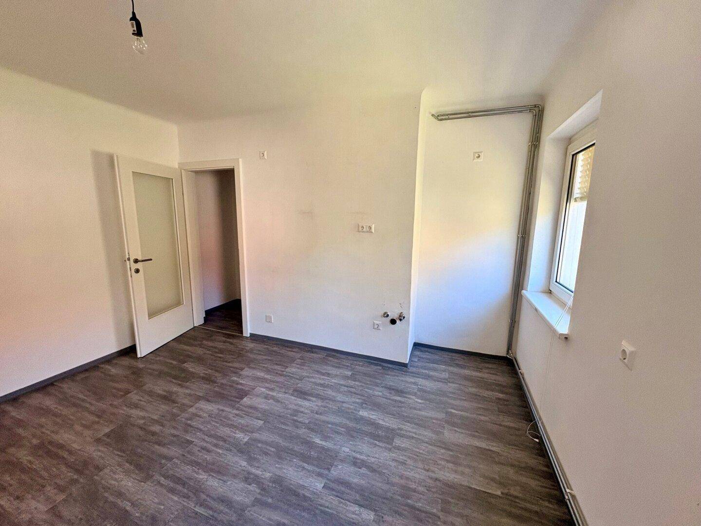 Leerer Raum, vorbereitet für eine Küche, mit Laminatboden und Fenster.