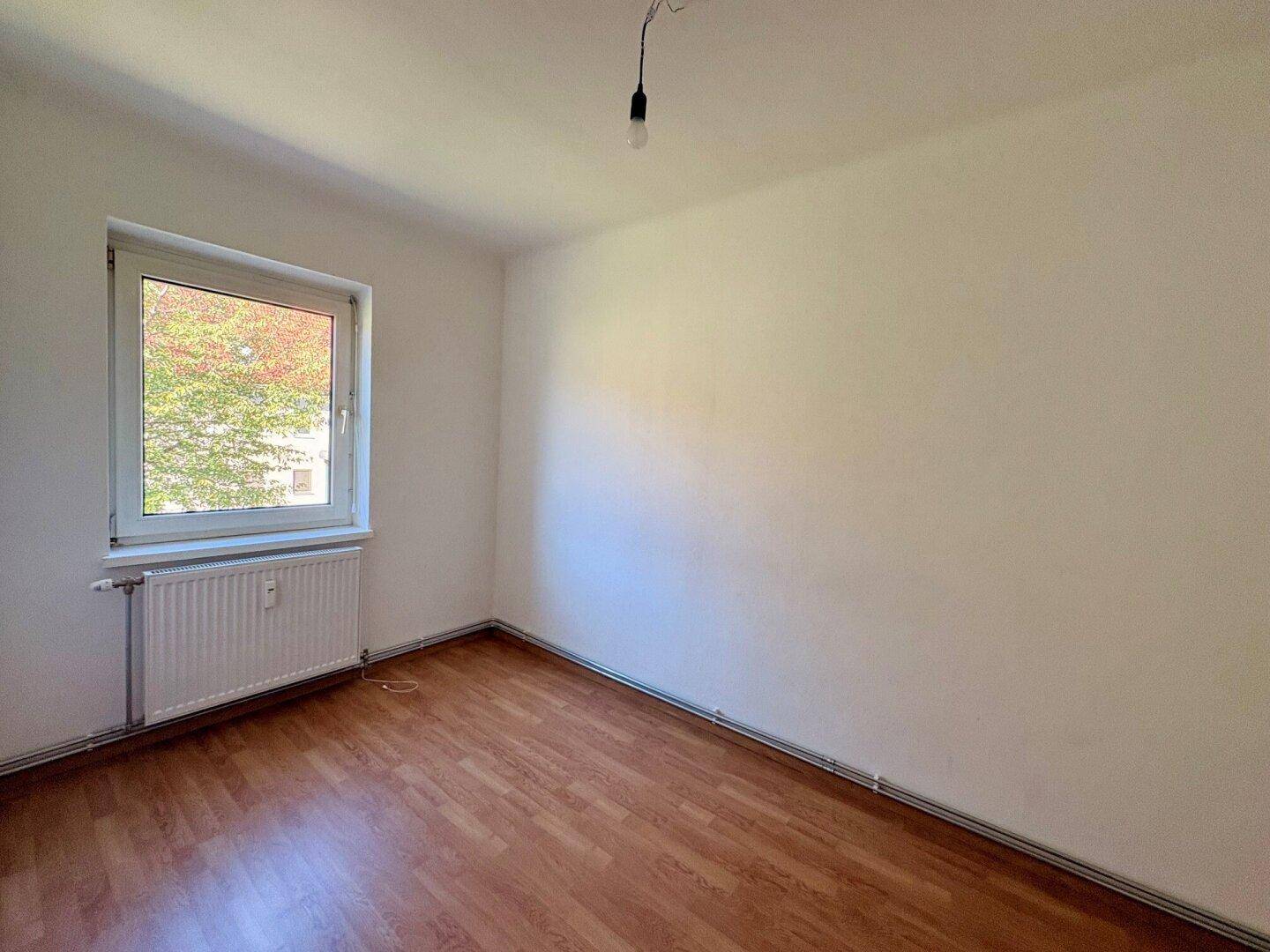 Leeres Schlafzimmer mit Laminatboden, weiß gestrichenen Wänden und einem Fenster.