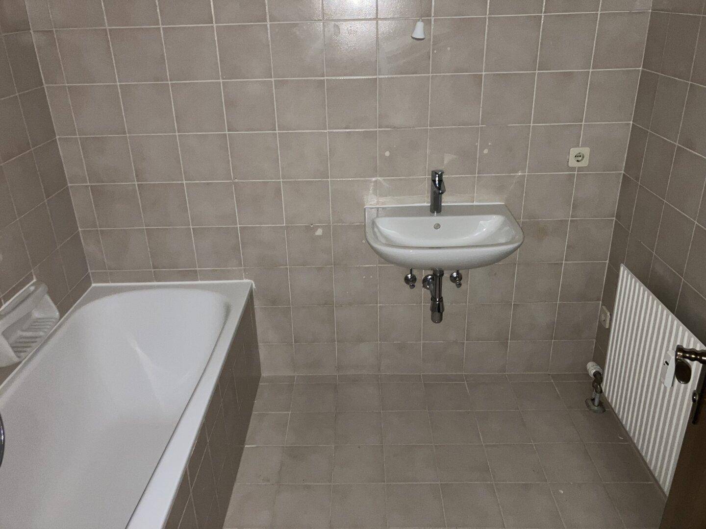 Badezimmer mit beigen Fliesen, einer Badewanne und einem Waschbecken, funktional und sauber.