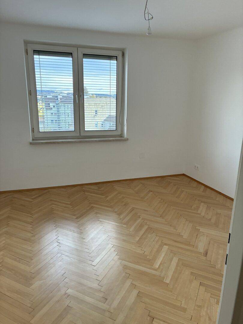 Helles Zimmer mit Fischgrätparkettboden und großem Fenster, das einen weiten Blick bietet.
