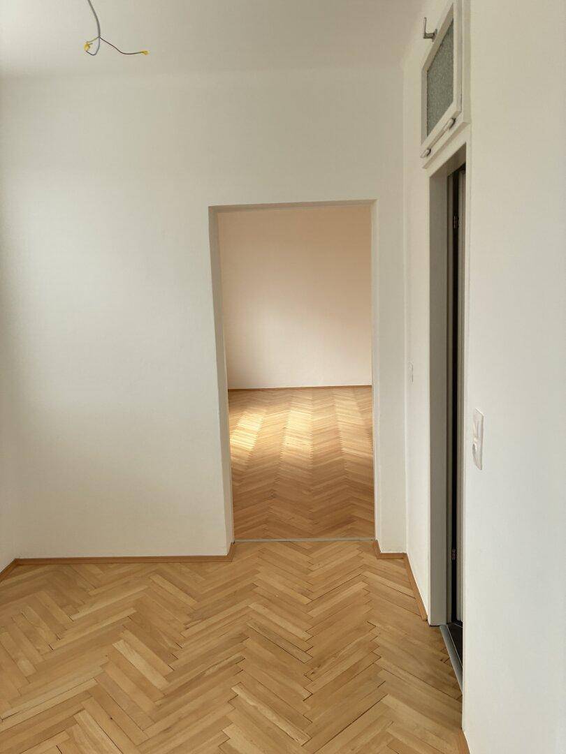Heller Übergangsbereich mit Fischgrätparkettboden, der zu einem weiteren Zimmer führt.