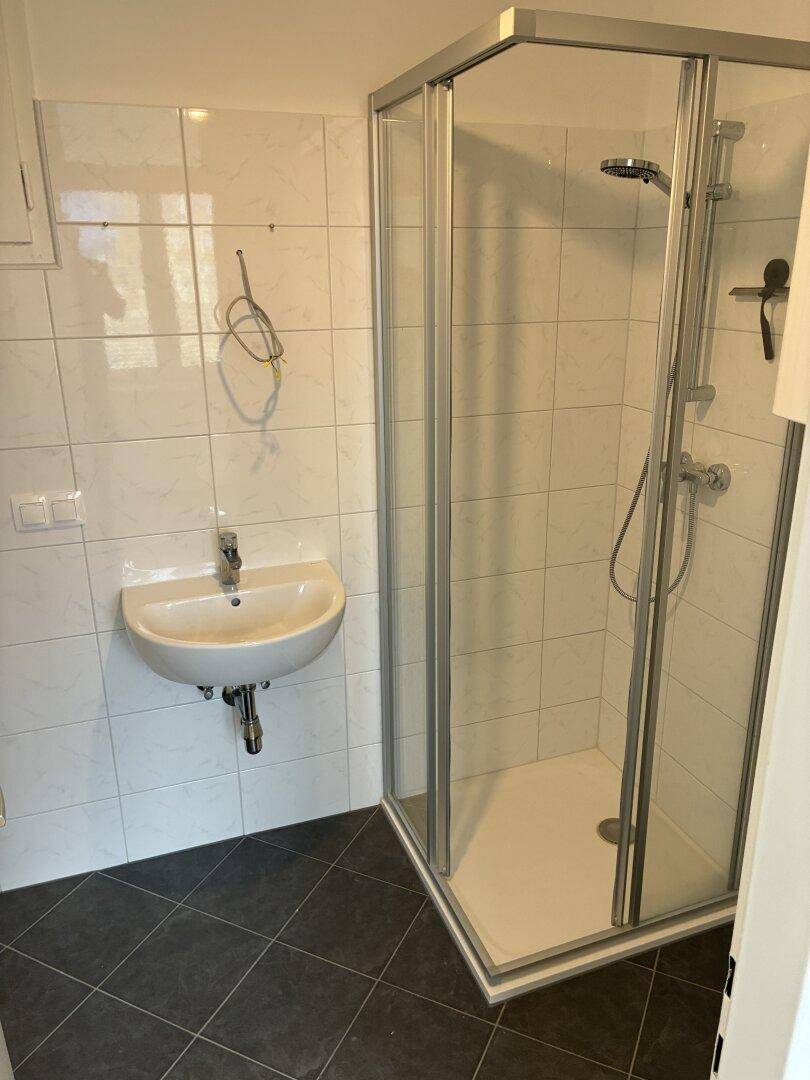 Modernes Badezimmer mit weißen Fliesen, dunklem Boden und einer verglasten Duschkabine.