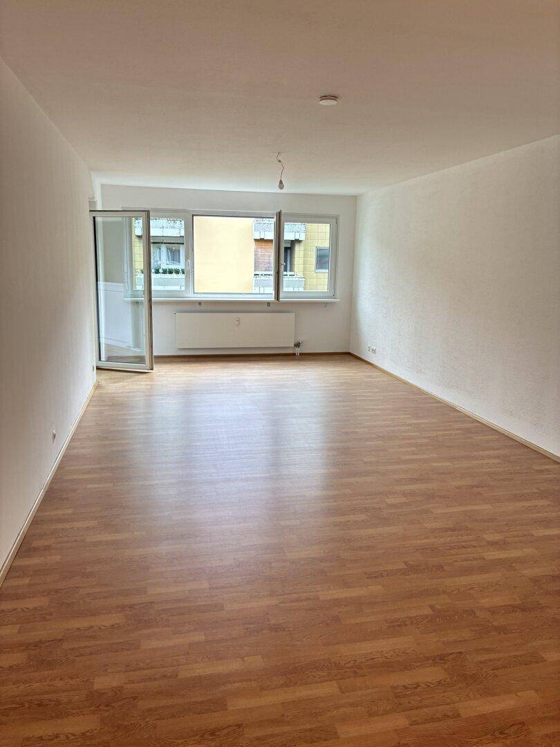 Geräumiges Wohnzimmer mit hellem Laminatboden und großen Fenstern für viel Tageslicht.