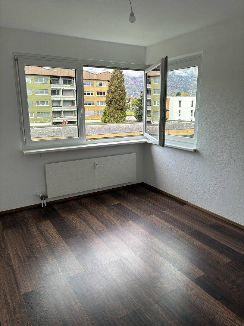 Schlafzimmer mit dunklem Laminatboden und weitem Blick auf die umliegenden Gebäude und Berge.
