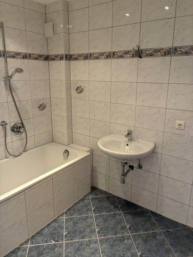 Badezimmer mit Badewanne, Duschfunktion, Waschbecken und blauen Bodenfliesen.
