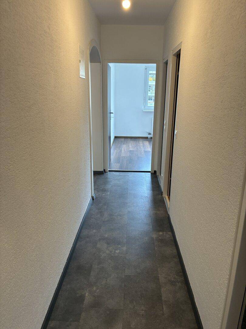 Langer, schmaler Flur mit dunklem Fliesenboden und Zugang zu weiteren Räumen.