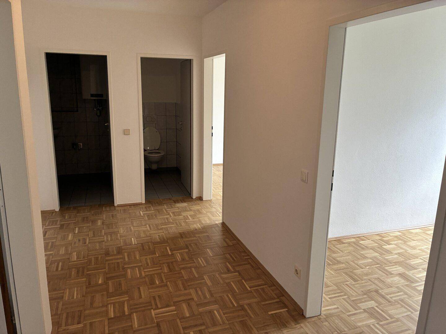 Heller Flur mit Parkettboden und Türen, die zu Badezimmer und separatem WC führen.