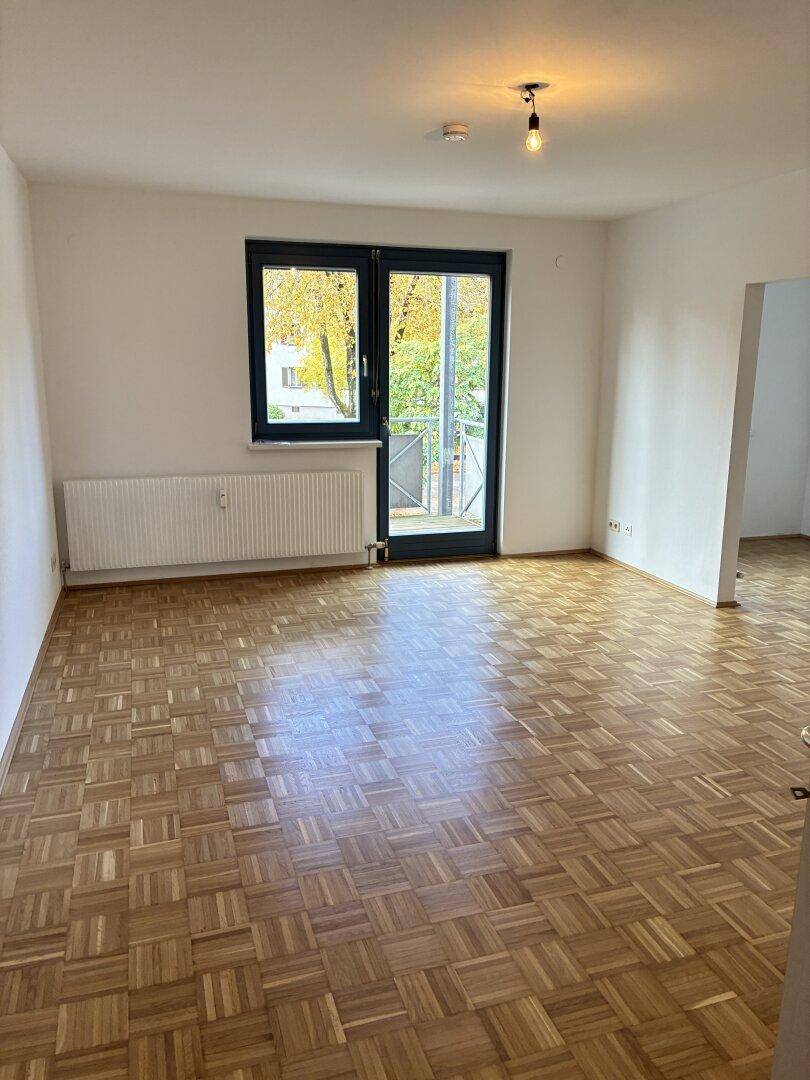 Geräumiges Wohnzimmer mit Parkettboden, Heizkörper und Zugang zu einem Balkon.