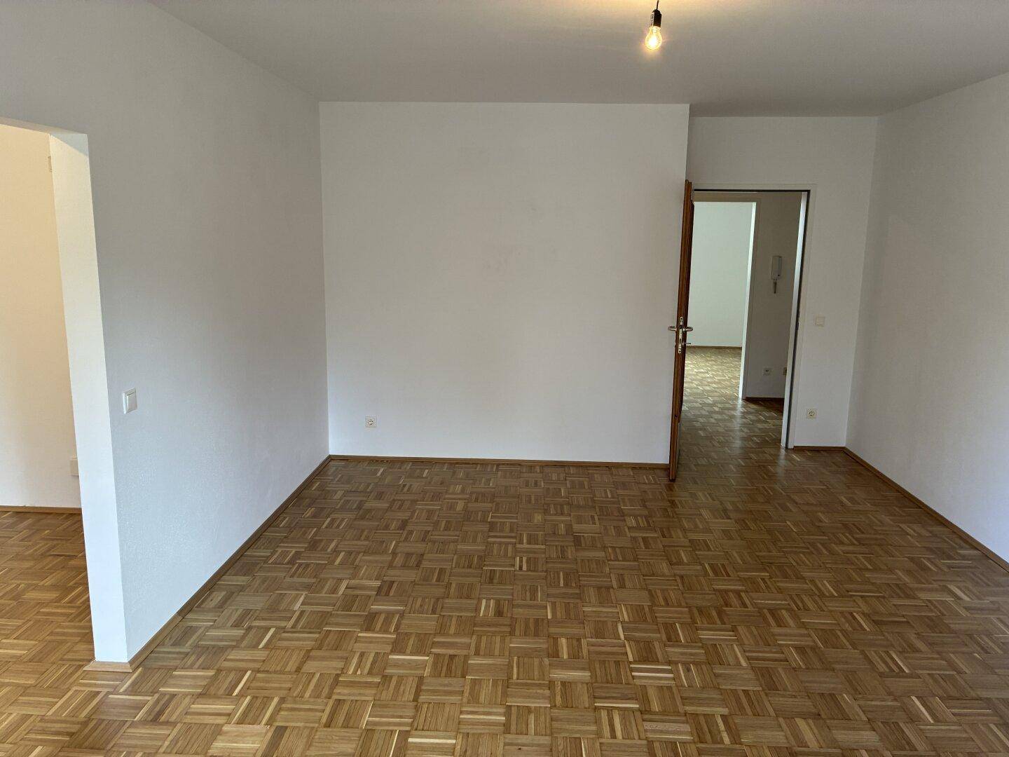 Heller Raum mit Parkettboden und weiß gestrichenen Wänden, mit Türzugang.