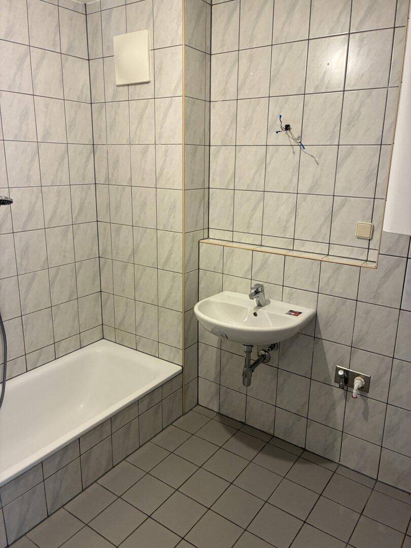 Gefliestes Badezimmer mit Badewanne, Waschbecken und hellen Wandfliesen im 80er-Jahre-Stil.