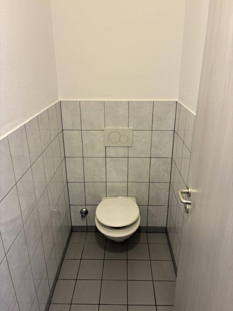Kleines, gefliestes WC mit Toilette und Spülkasten in neutralen Farben im 80er-Jahre-Stil.