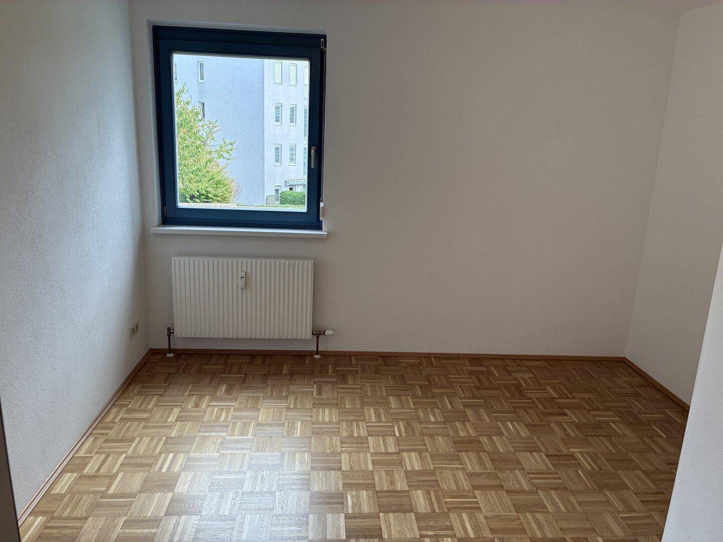 Geräumiges Schlafzimmer mit Parkettboden, Heizkörper und Blick auf ein Nachbargebäude.