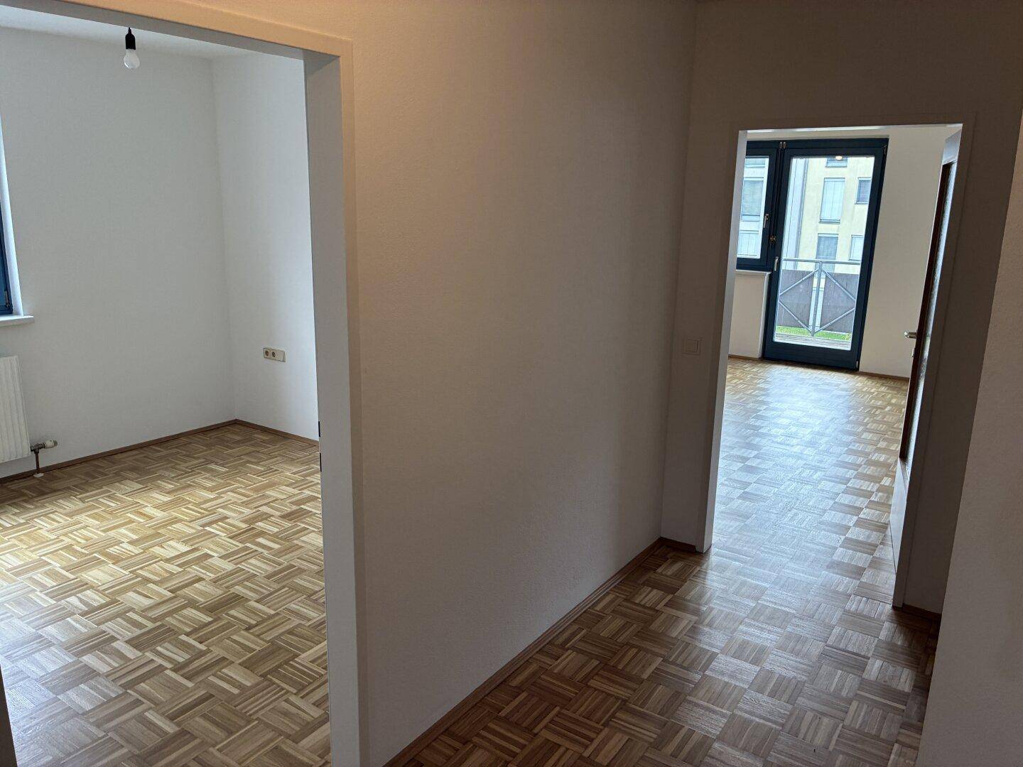Heller Flur mit Parkettboden, der zu verschiedenen Räumen und einem Balkon führt.