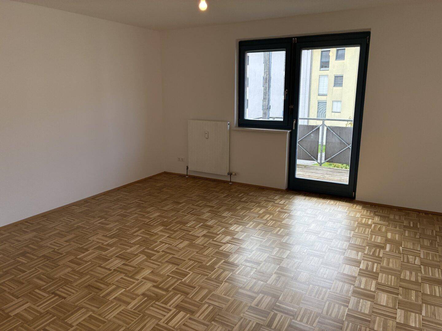 Geräumiges Zimmer mit Parkettboden und Zugang zu einem Balkon oder einer Terrasse.