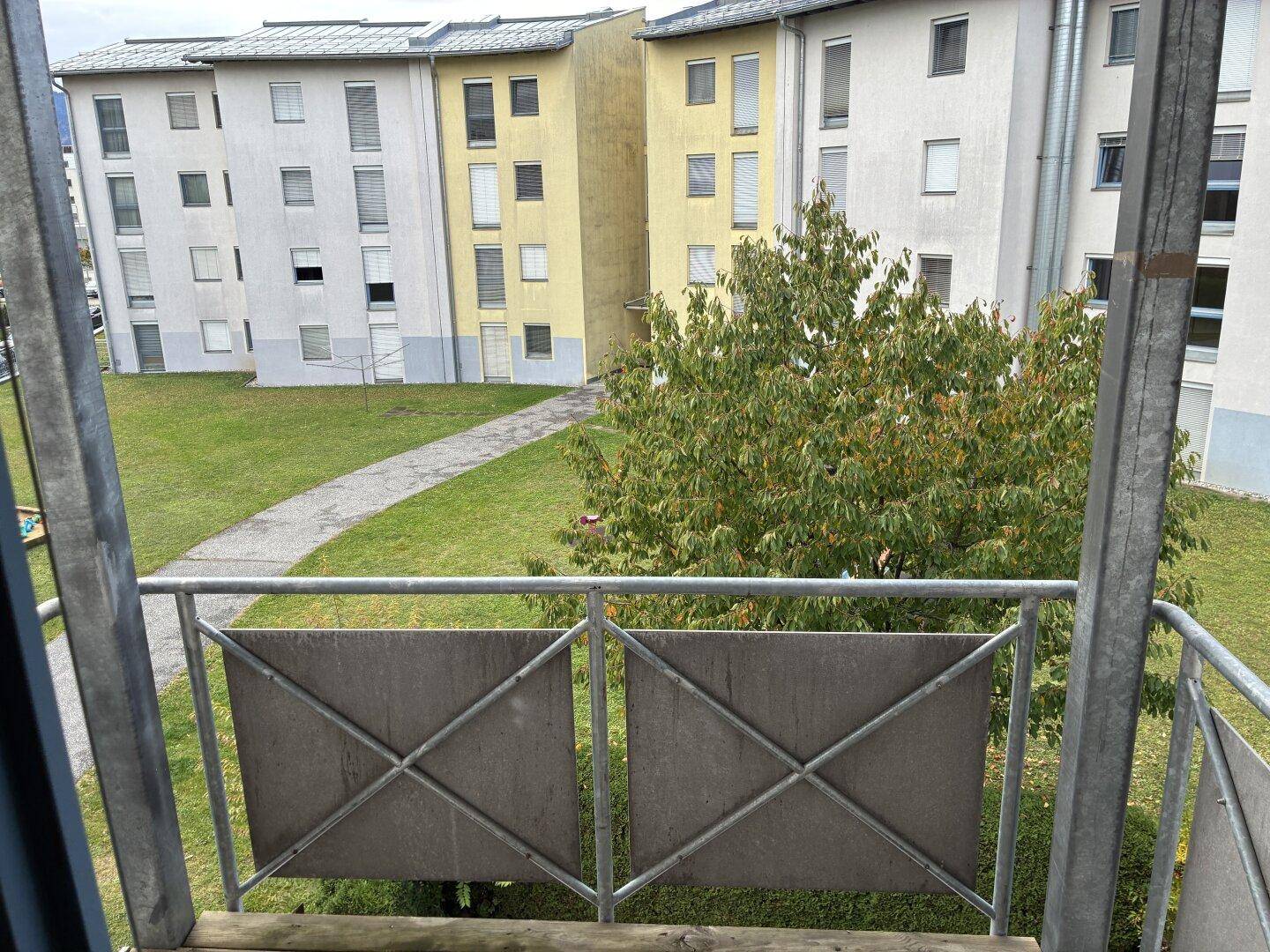 Blick von einem Balkon auf den grünen Innenhof und umliegende Wohngebäude.