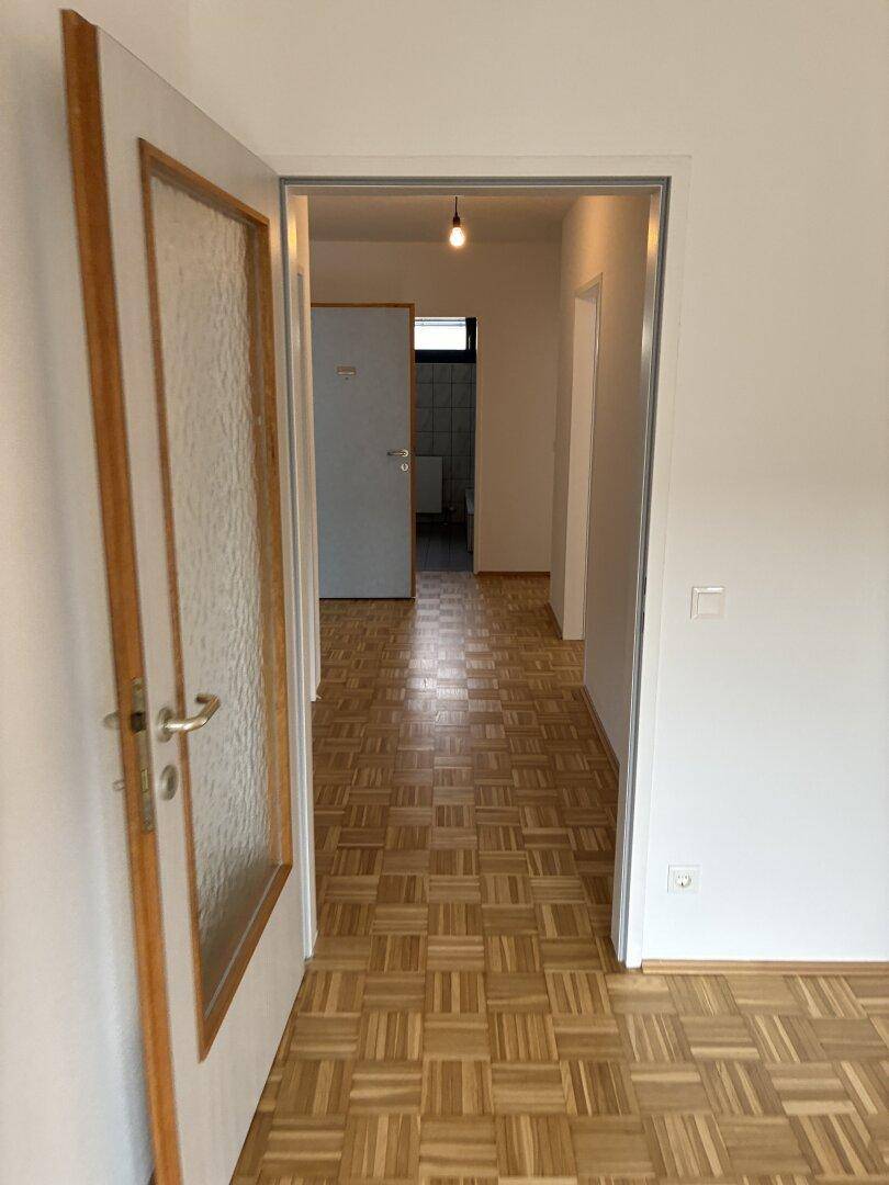 Langer Flur mit Parkettboden, der zu einem Badezimmer und weiteren Zimmern führt.