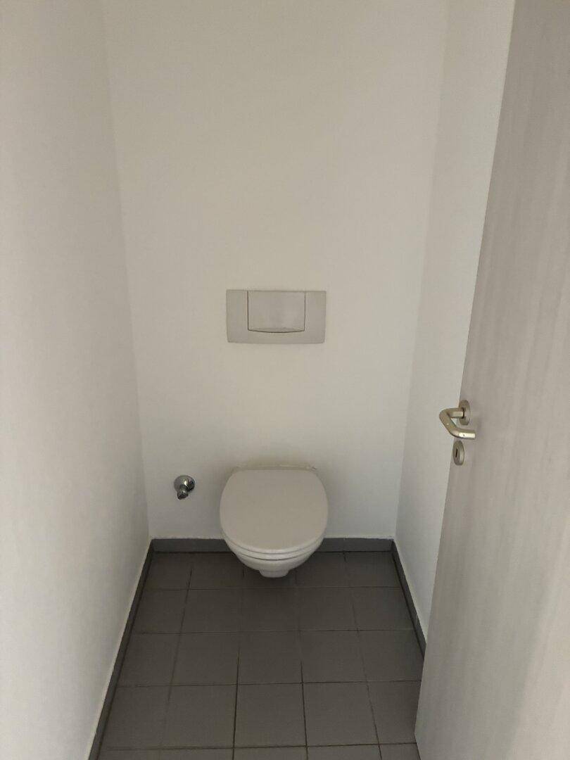 Kleines, funktionales WC mit Wand-WC und dunklen Fliesen auf dem Boden.