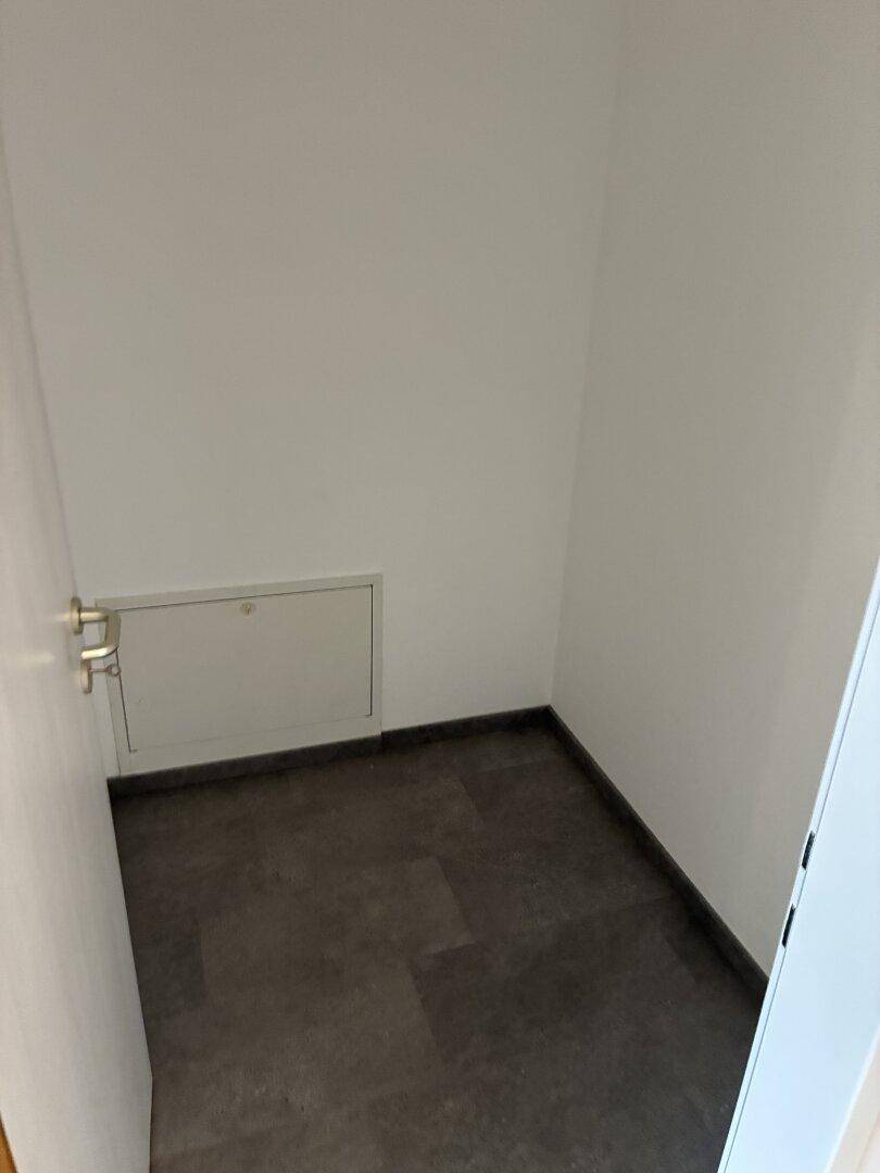 Praktischer Abstellraum mit dunklem Boden und einer Wartungsklappe an der Wand.