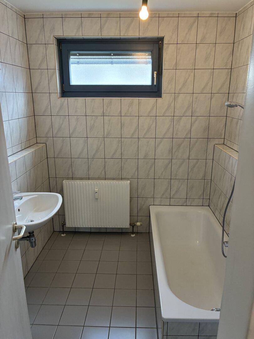 Badezimmer mit Badewanne, Waschbecken, Fenster und hellen Wandfliesen.