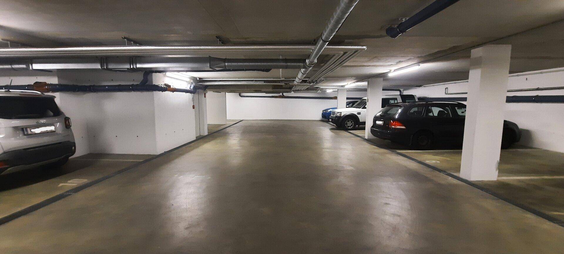 Lange Tiefgarage mit mehreren Parkplätzen und geparkten Fahrzeugen, gut beleuchtet.