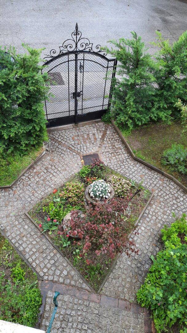 Vogelperspektive auf einen gepflasterten Gartenweg, Blumenbeete und ein schmiedeeisernes Tor.