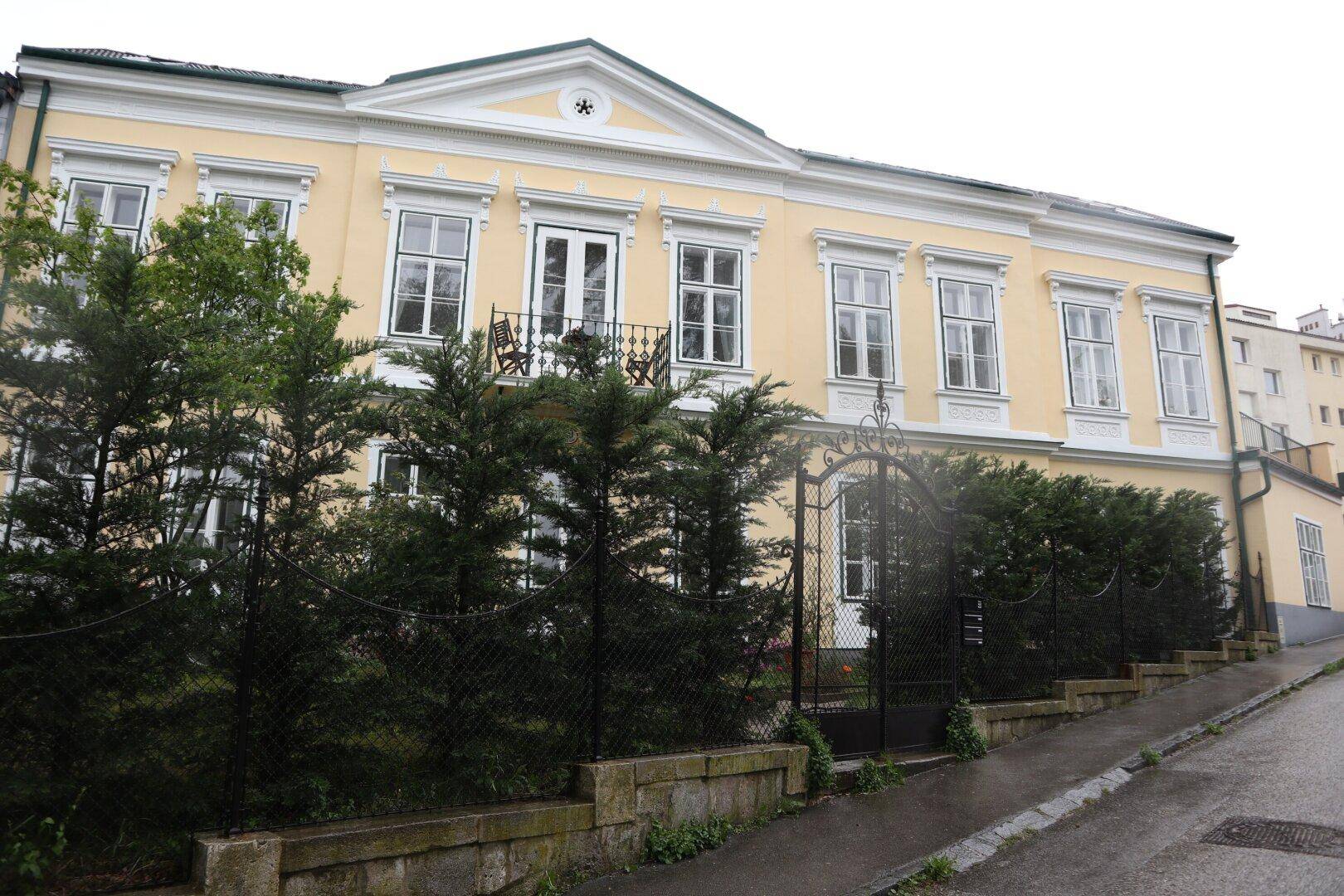 Historisches Gebäude mit gelber Fassade, umzäuntem Vorgarten und schmiedeeisernem Tor.