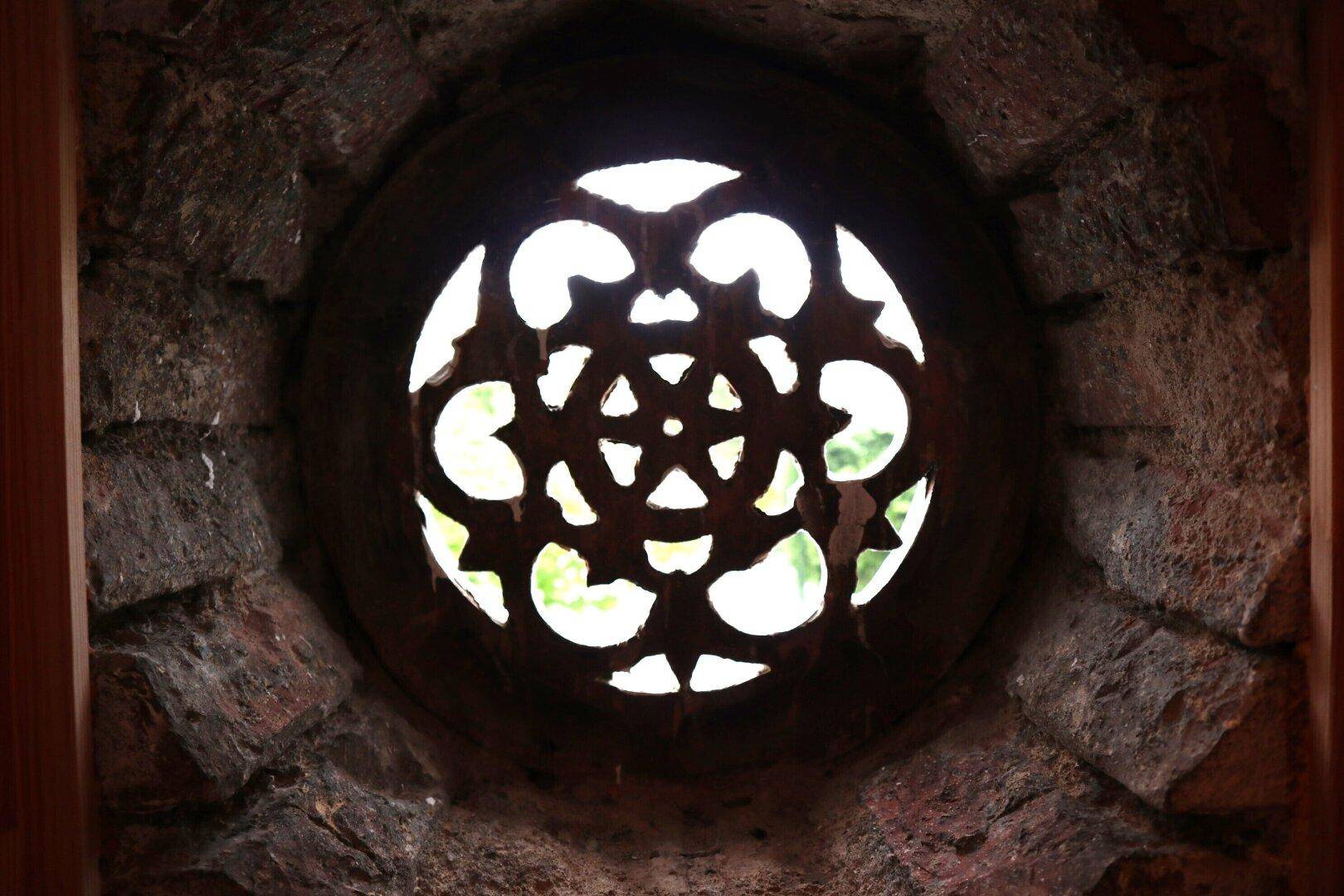 Rundes, kunstvoll geschnitztes Fenster in einer rustikalen Steinwand, das Licht hereinlässt.