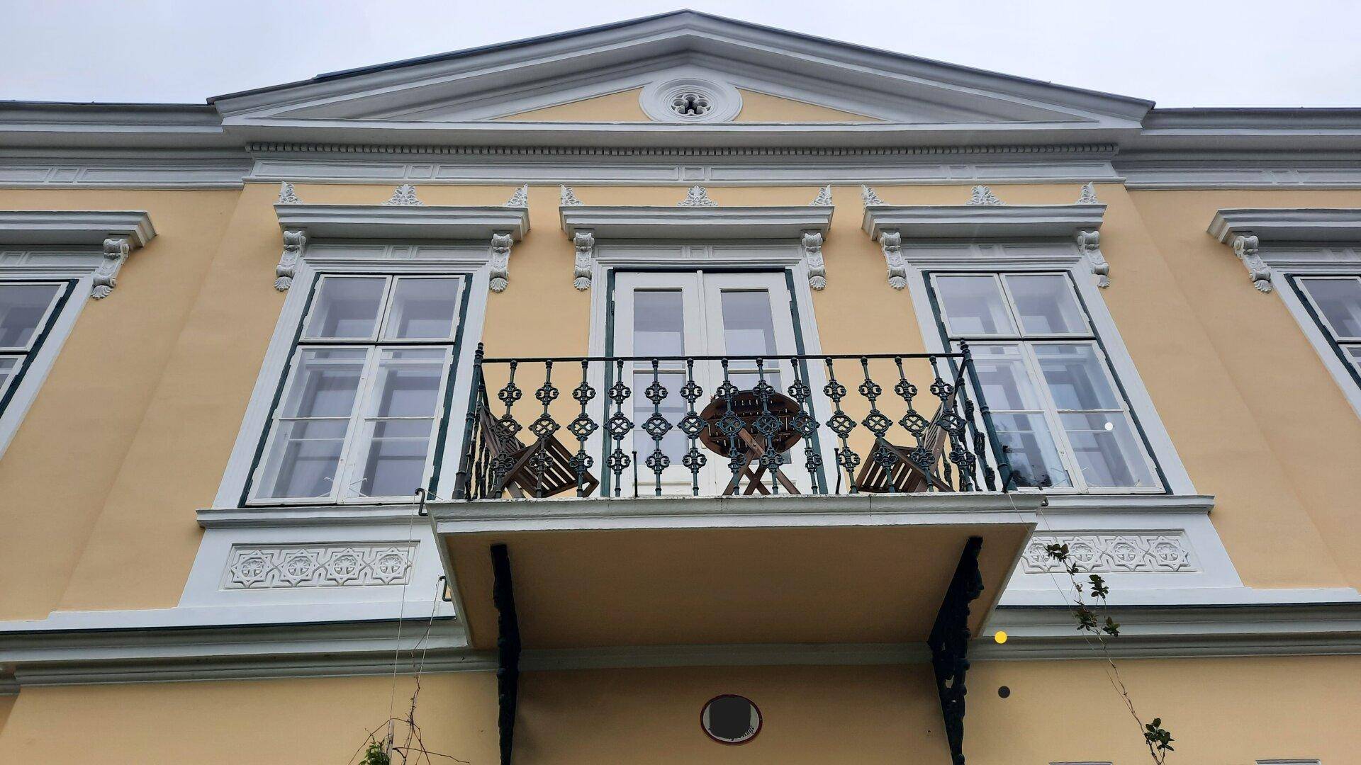 Kleiner Balkon mit schmiedeeisernem Geländer und Sitzgelegenheiten an der historischen Fassade.