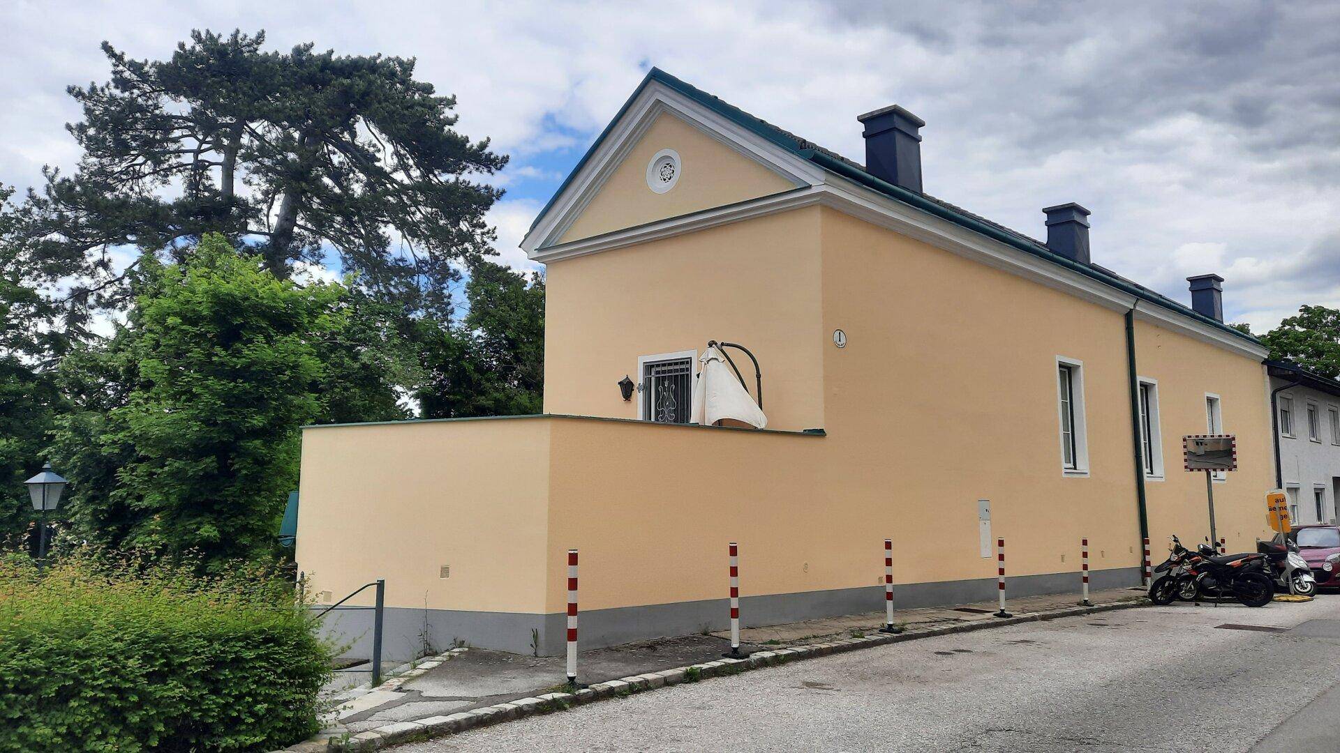 Seitenansicht des historischen Gebäudes mit gelber Fassade und grünen Bäumen im Hintergrund.
