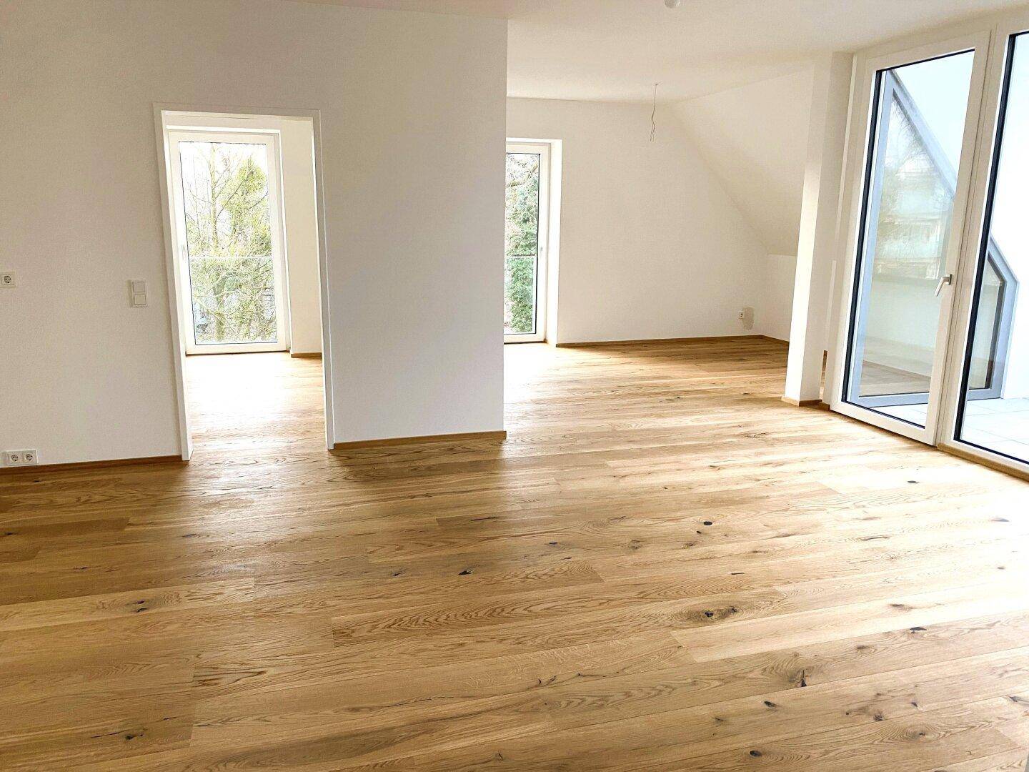 Lichtdurchfluteter Wohnbereich mit Holzboden, hohen Decken und Zugang zu mehreren Fenstern.